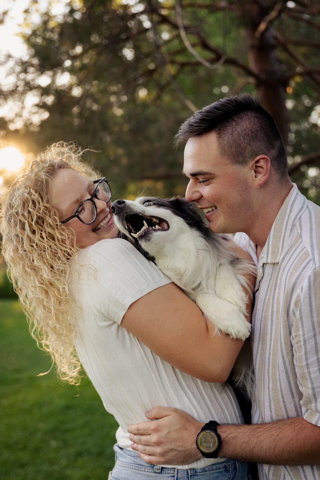 Couple smiling while holding their dog in a warm sunset embrace