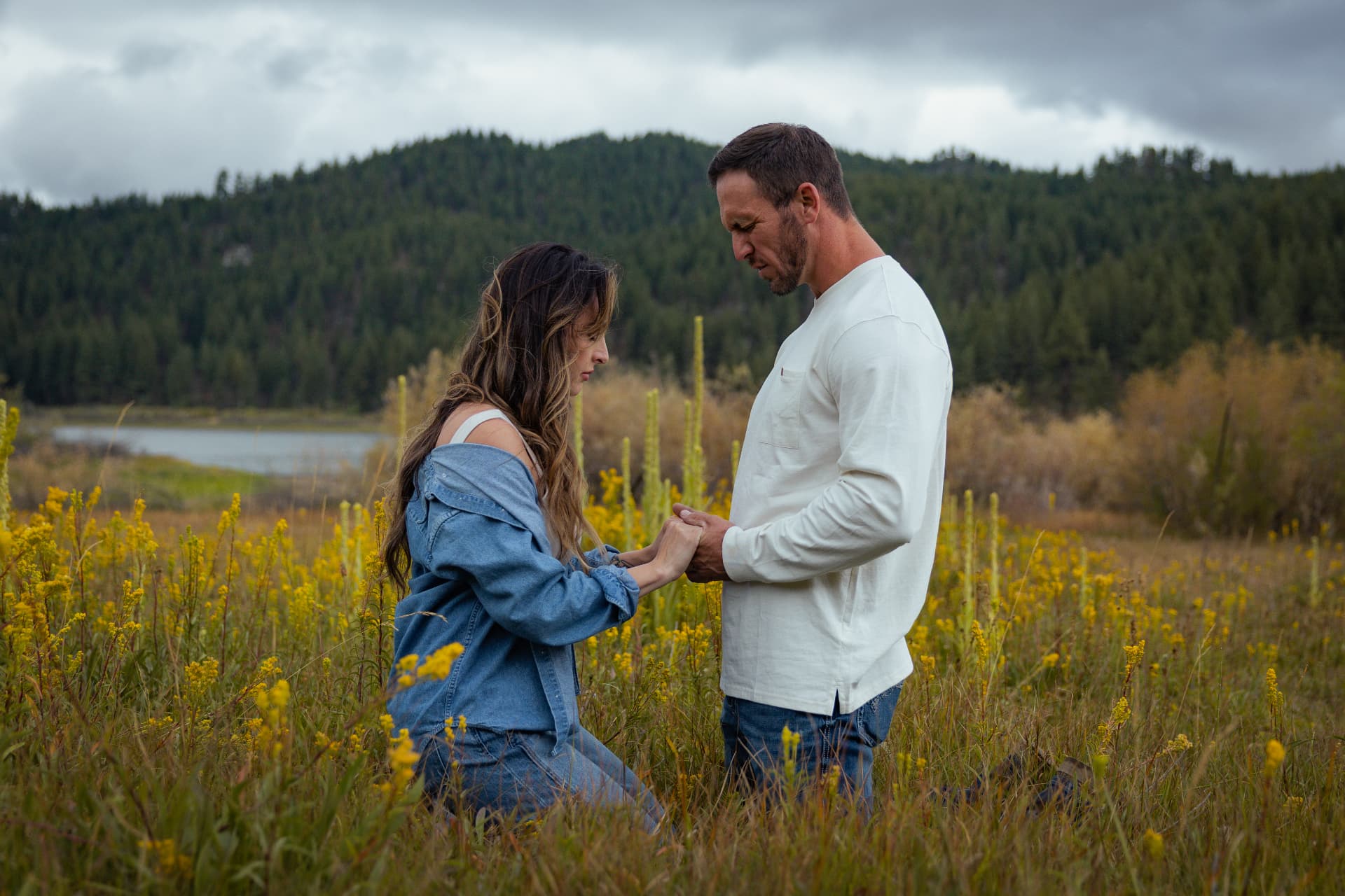 Couple kneeling face to face holding hands in a meadow of yellow wildflowers