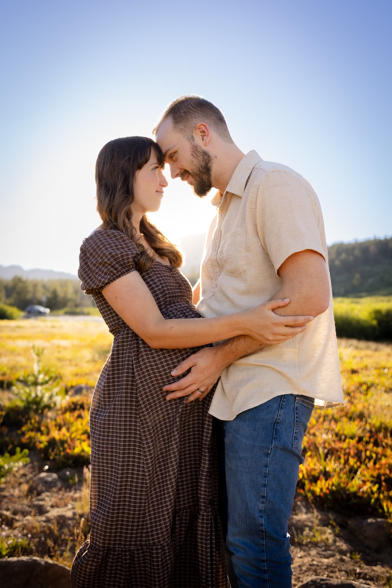 Expecting couple forehead to forehead in a sunlit mountain meadow