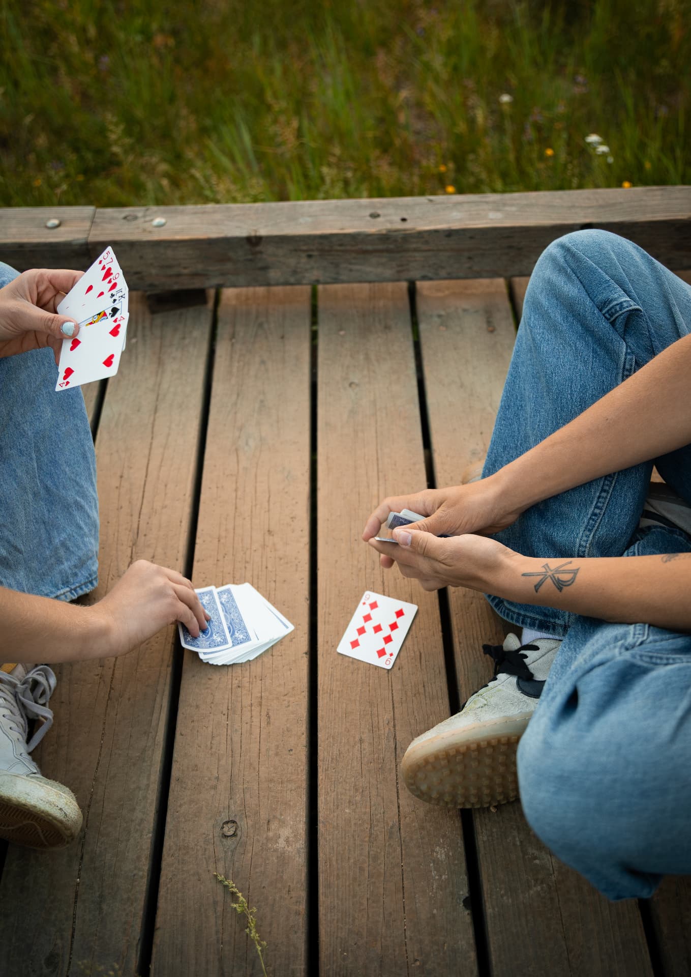 Overhead detail of a couple playing cards on a wooden dock beside tall grass