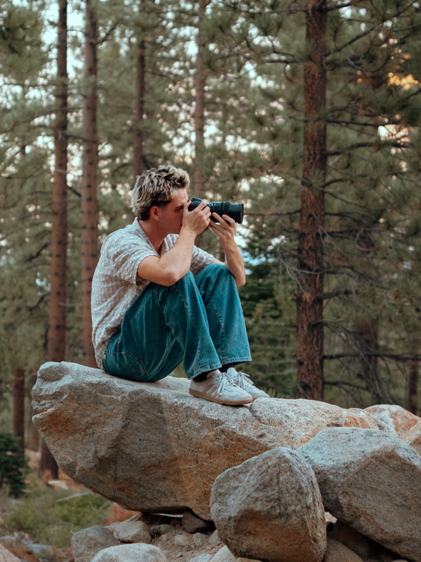 David, the photographer behind DavidBVisuals, sitting on a rock with his camera in the Tahoe woods