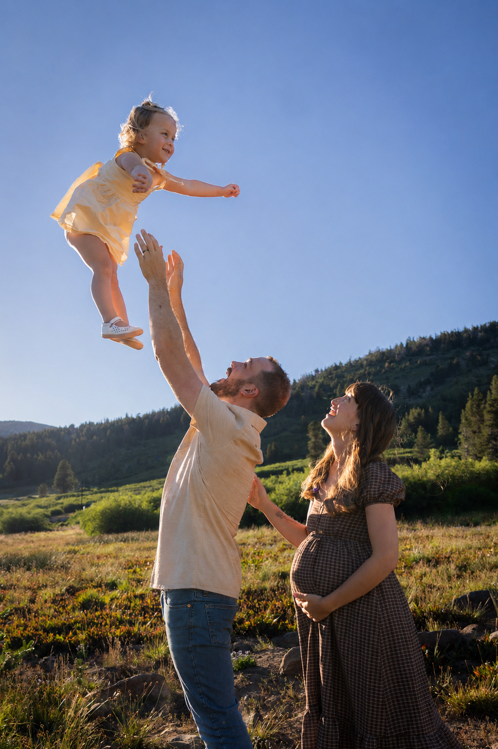 Father tossing his toddler daughter into the air in a mountain meadow at golden hour
