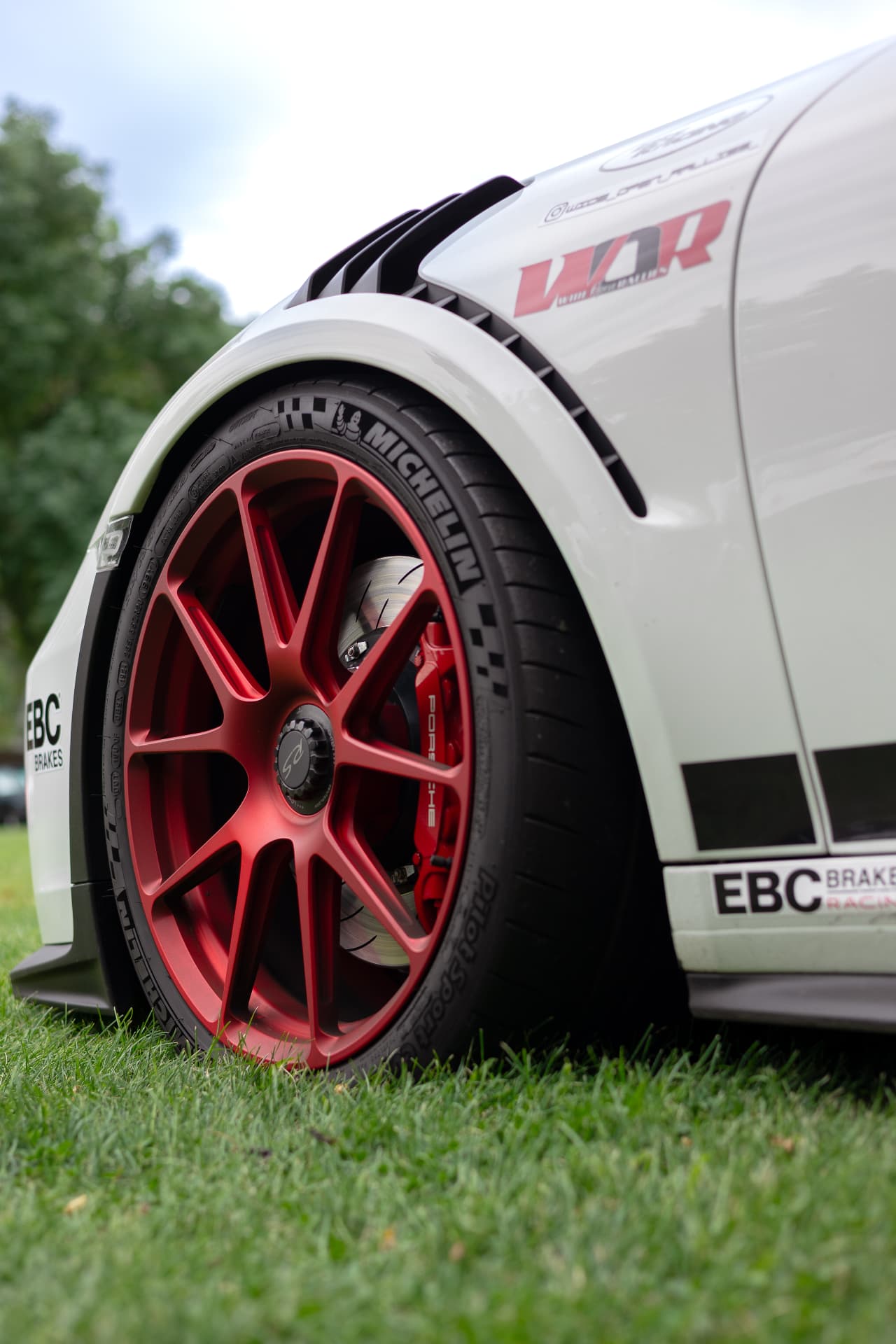 Low angle of a white Porsche race car's red forged wheel and brake caliper on grass