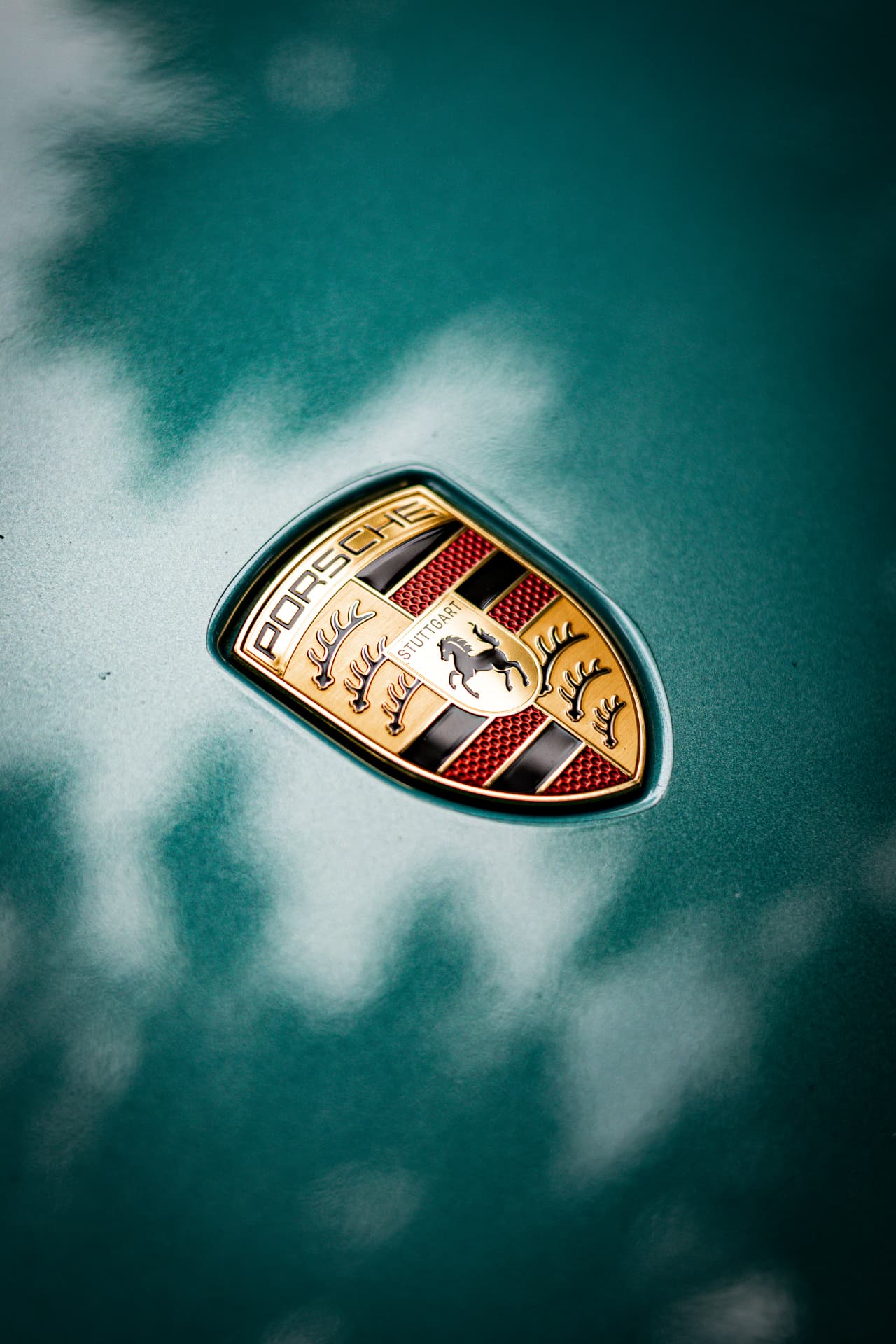 Close detail of a gold Porsche crest on a deep green metallic hood